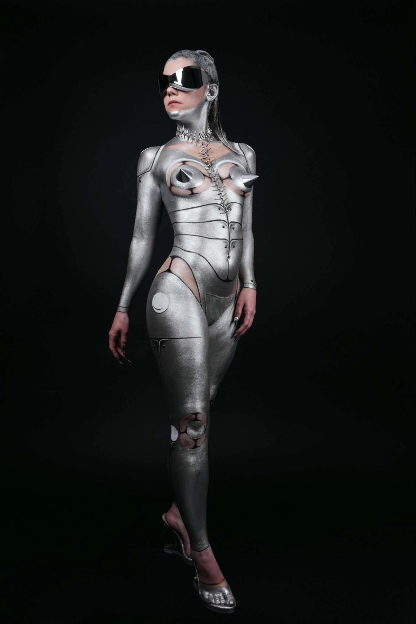 Body painting futuriste argenté aux volumes métalliques sur fond noir.